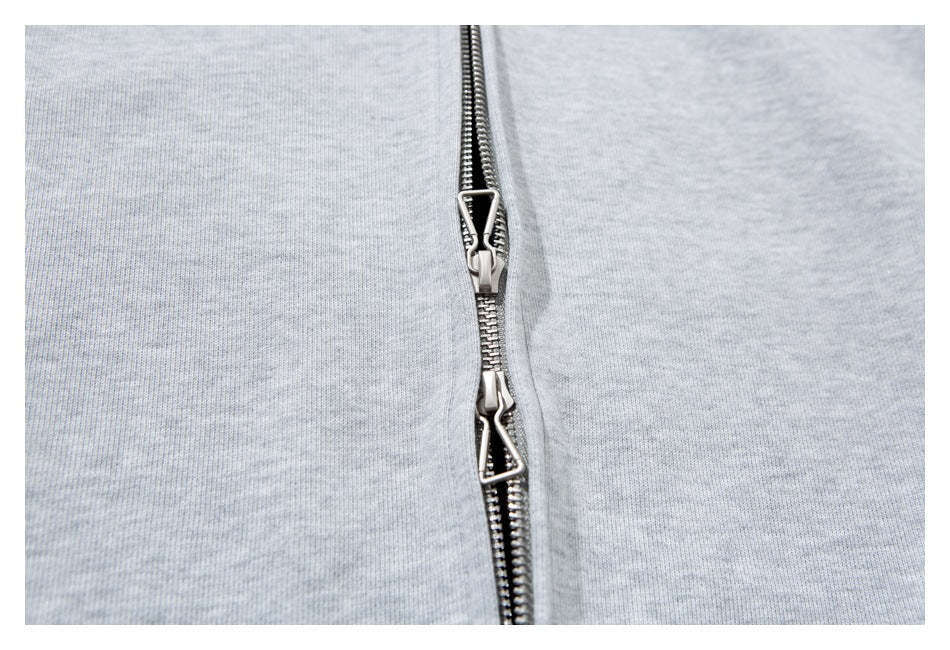 Macro view of two silver zipper pulls on a light gray heather sweatshirt.