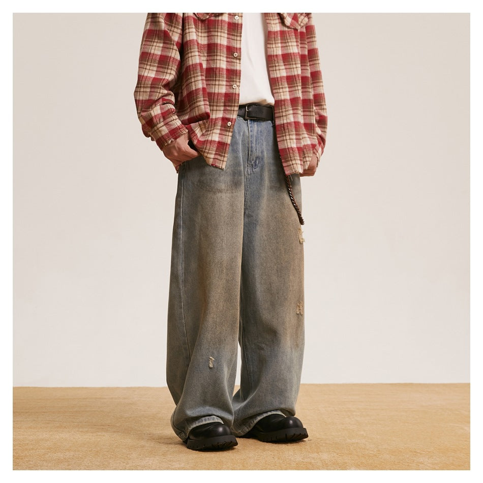 Cropped model wearing loose, faded gray-blue wide-leg jeans with small distressed patches and black chunky shoes.