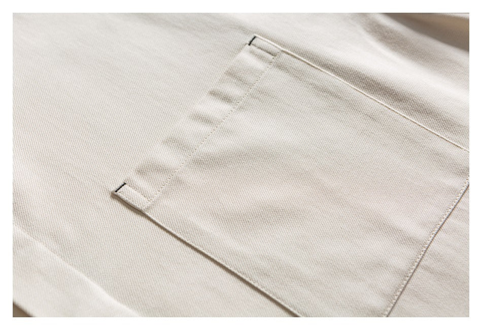 Close-up of a stitched rectangular pocket on a light beige garment.