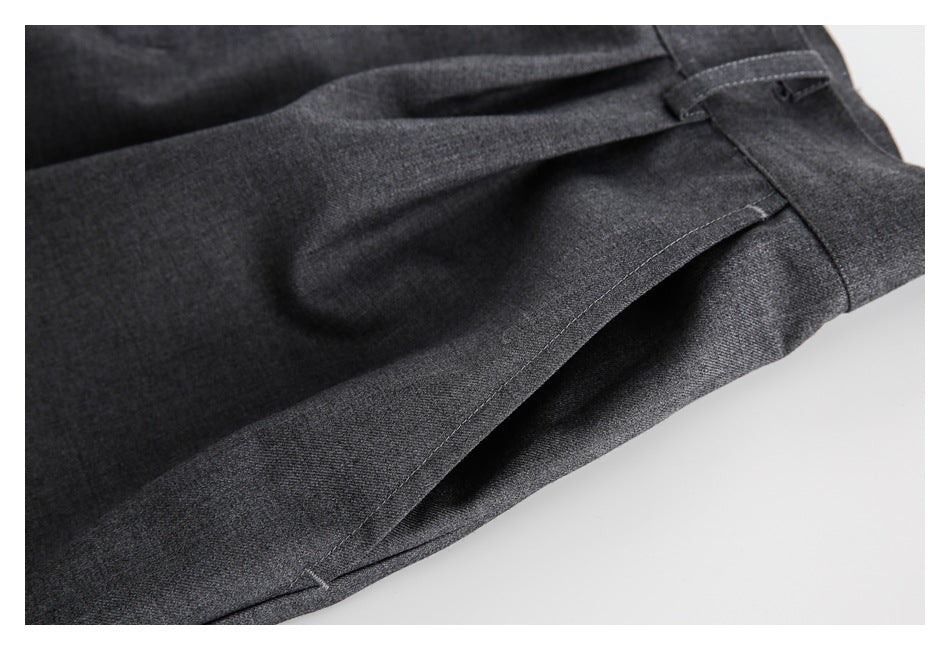 Close-up of charcoal gray trousers showing a folded pleat, belt loop, and stitched seams.