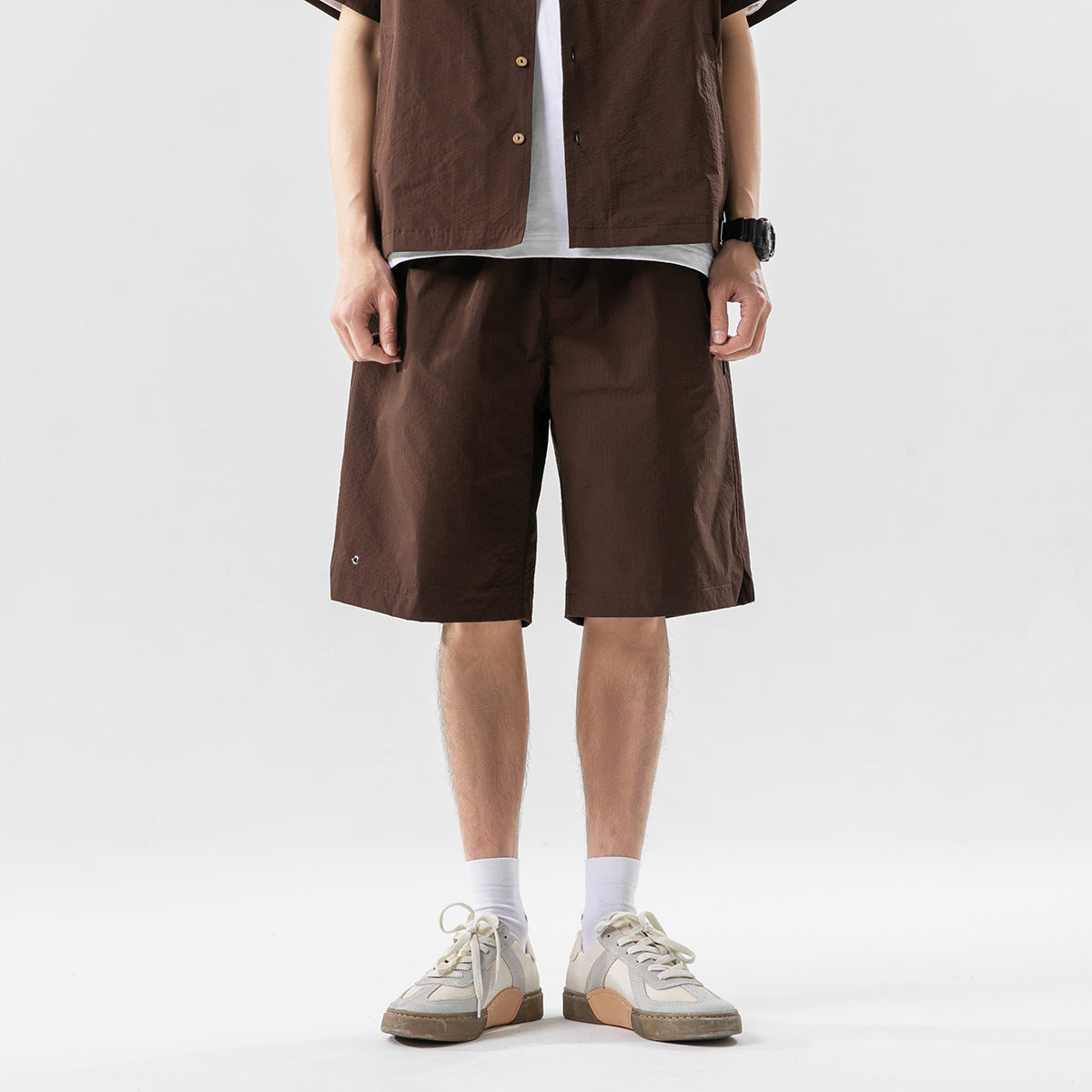Front view of a model wearing dark brown knee-length shorts with a matching button-front shirt.