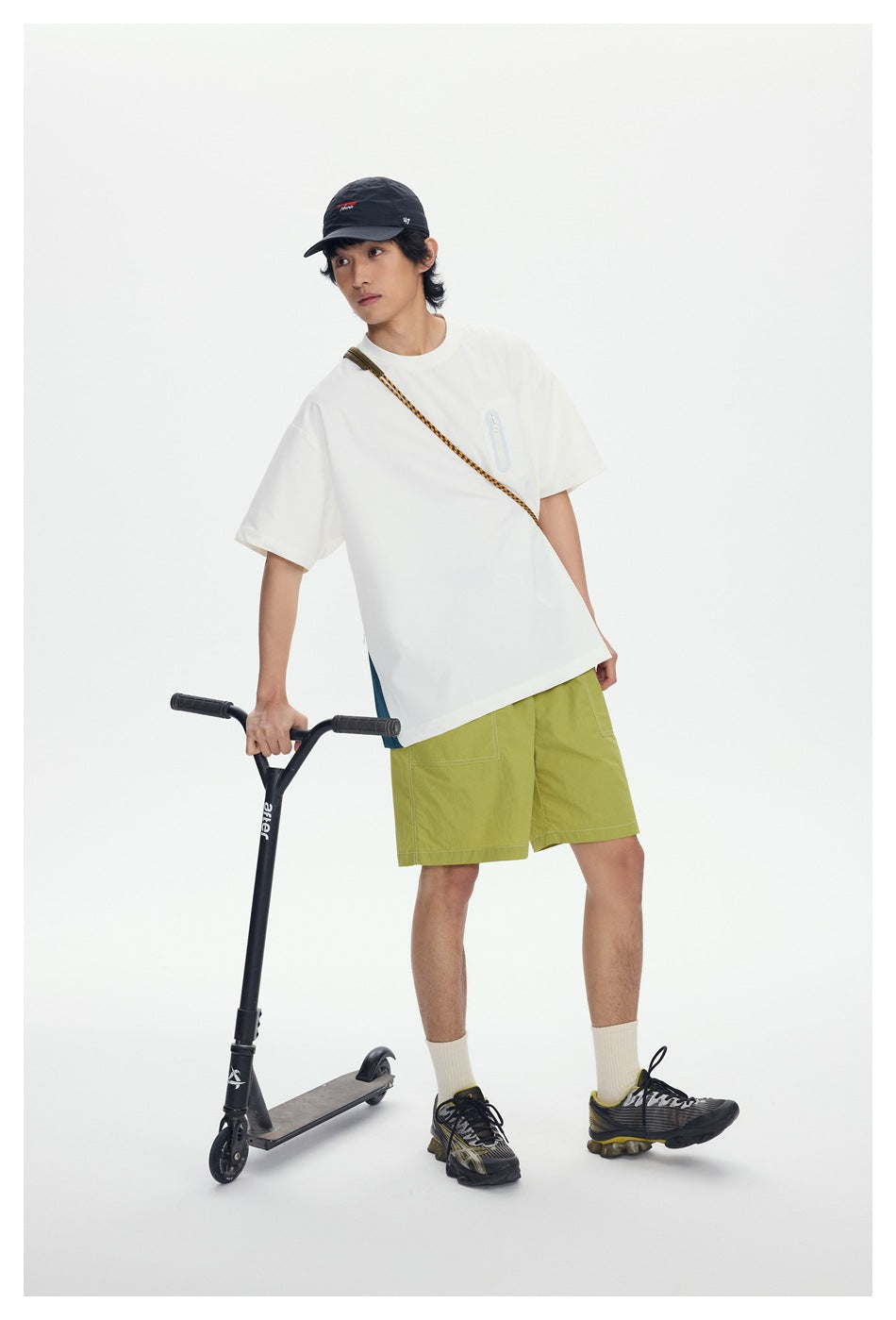 Model wearing a white T-shirt and lime-green shorts, leaning beside a scooter.