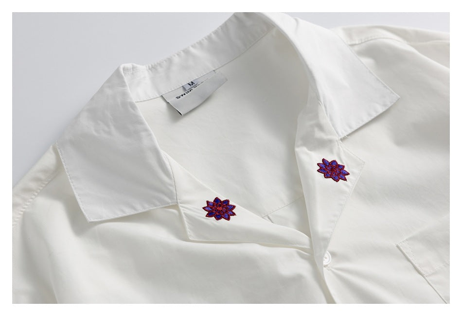 Close-up of a white shirt collar with purple and red floral embroidery on the lapels and a neck label.
