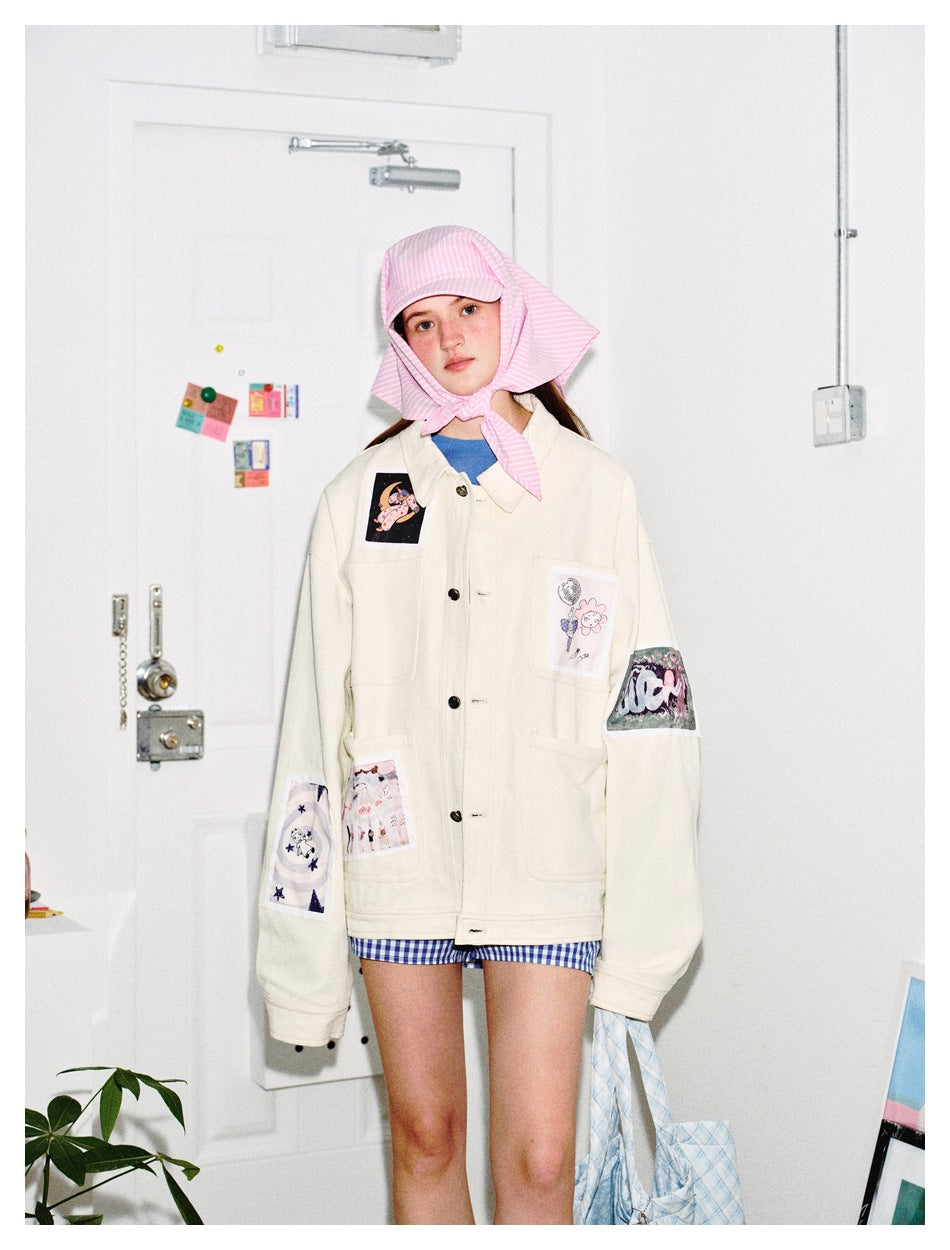 Front view of a model in an ivory jacket with illustrated patches, blue gingham shorts and a pink striped bonnet.