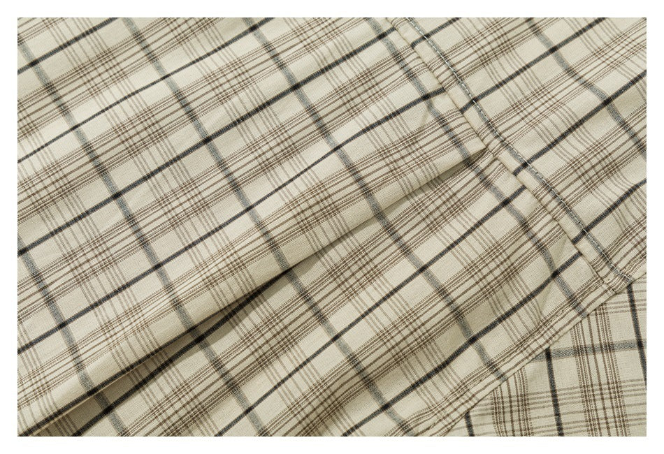 Close-up of cream fabric with a brown, charcoal, and gray plaid pattern, folded to show a stitched edge.