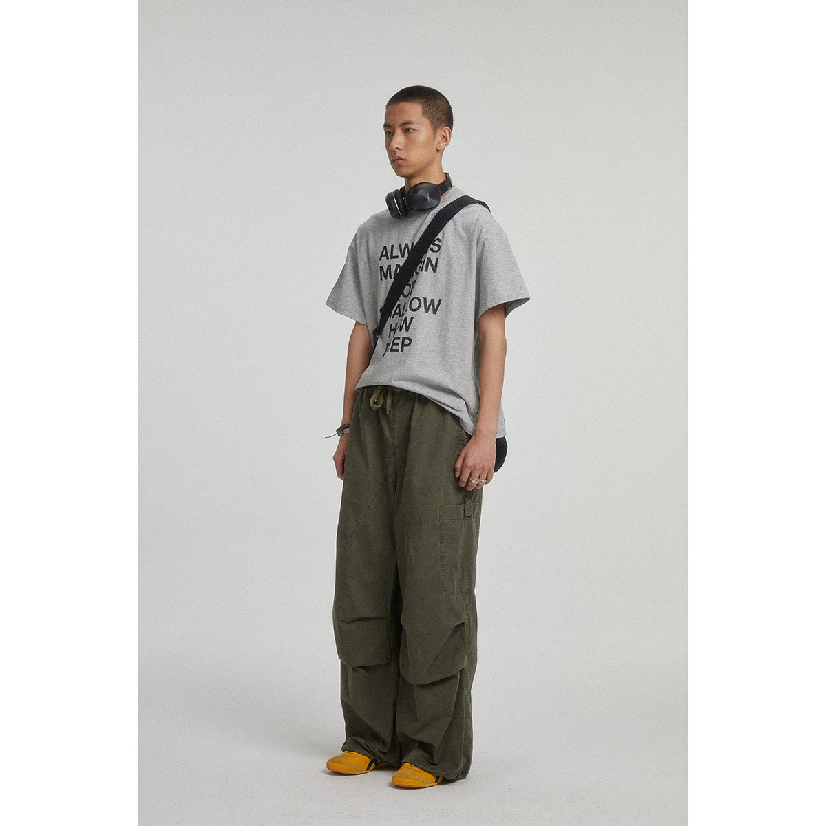 Model wearing a gray text-print T-shirt and loose olive cargo pants with oversized knee panels.