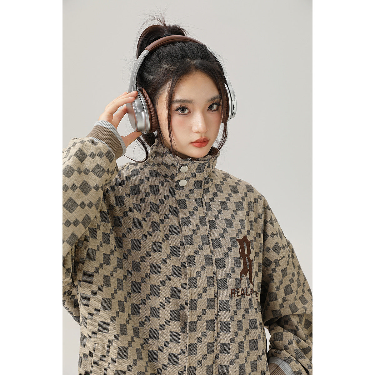 Close view of a model wearing a beige-and-charcoal geometric checker jacket with a stand collar and chest lettering.