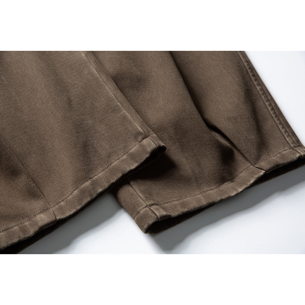 Close-up of the stitched hems on brown trousers.