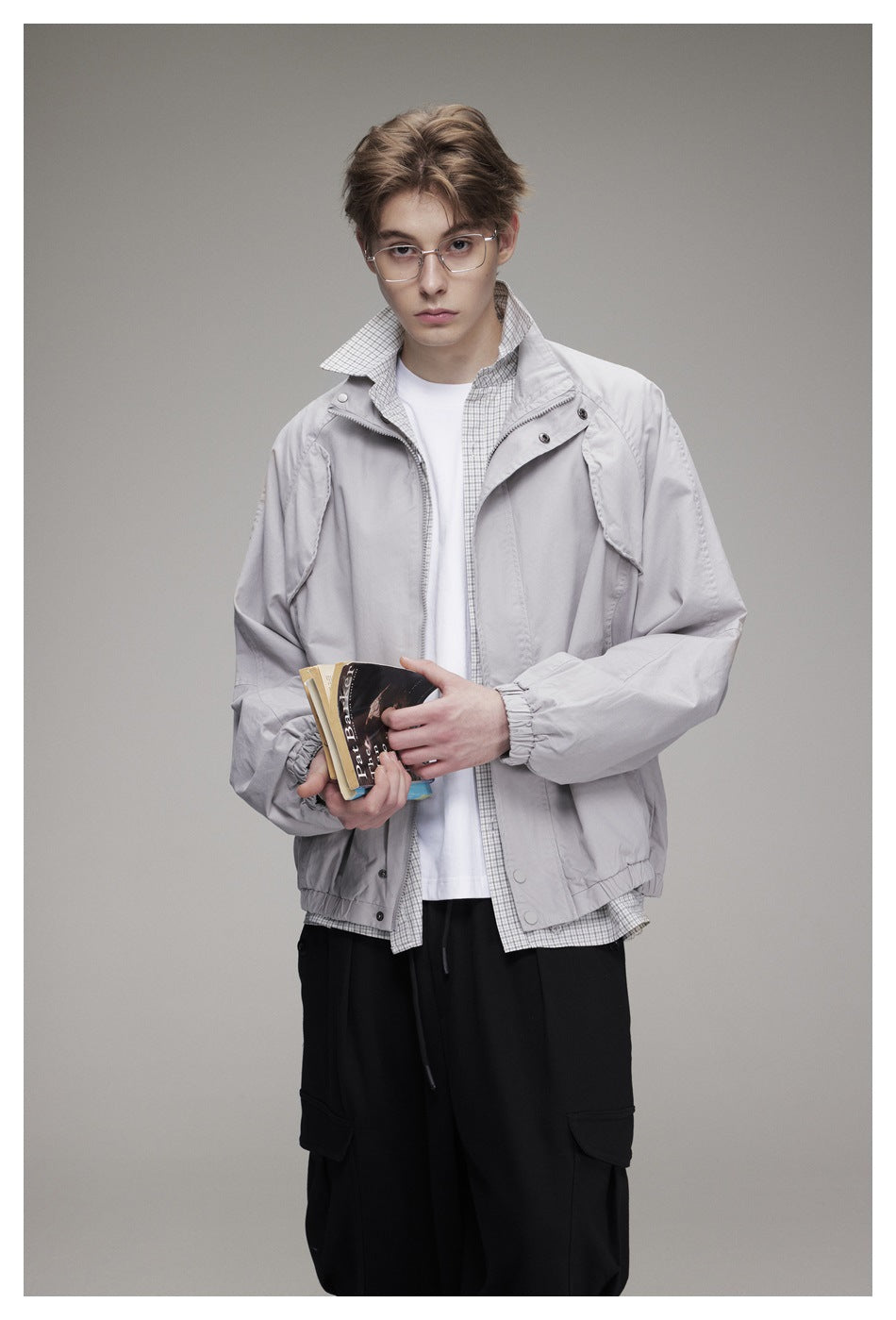 Model wearing a light gray zip-front jacket over a checked shirt and white tee, with black trousers.