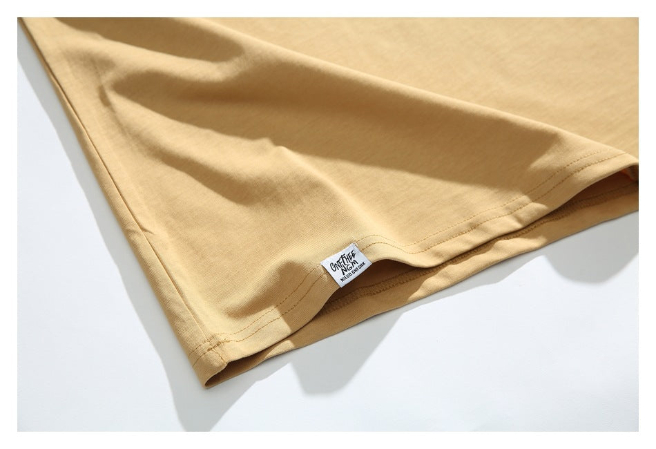 Close-up of the tan T-shirt's stitched hem and small sewn side label.