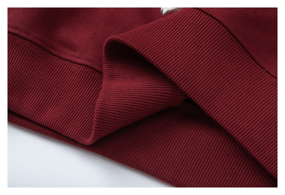 Close-up of burgundy ribbed sweatshirt bands and folded fabric, with a small partial white graphic at the top edge.