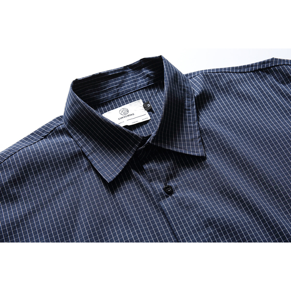 Close-up of a navy short-sleeve shirt with a fine white grid check, pointed collar, and front button.