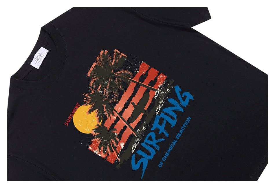 Angled view of a black T-shirt with a colorful sunset, palm tree and surfing graphic.