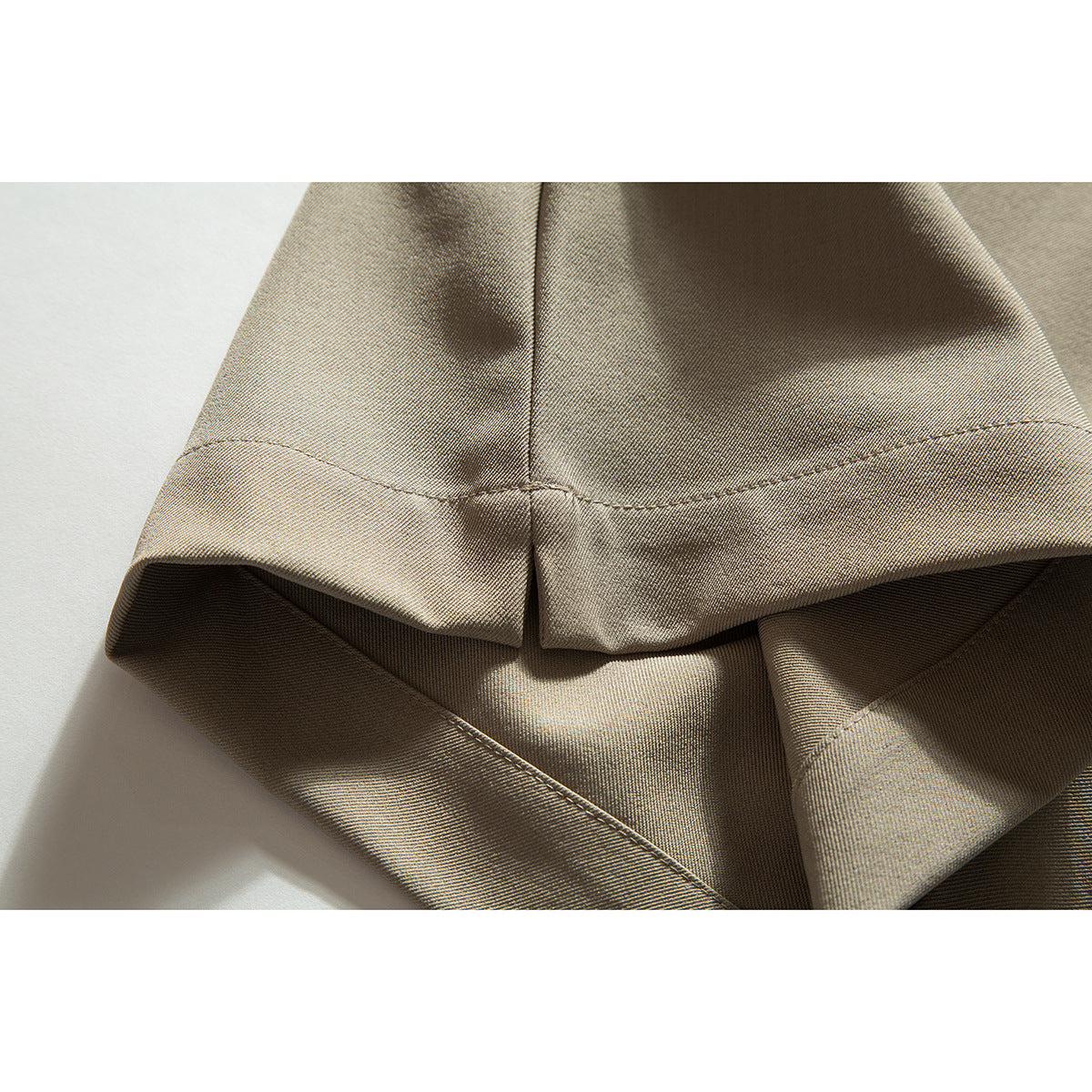 Close-up of the stitched hem and folded edge of beige shorts.
