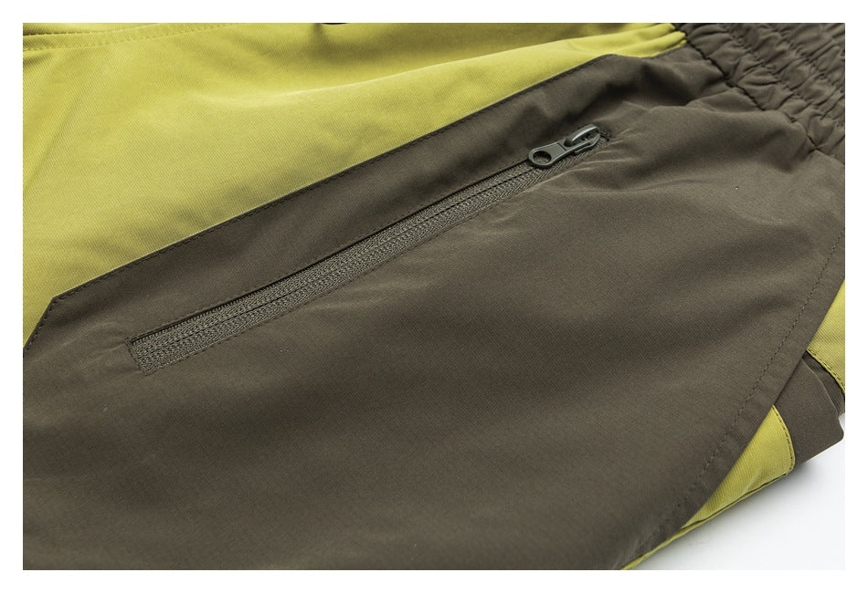 Close-up of a zippered pocket on olive shorts with chartreuse panels and an elastic waistband.