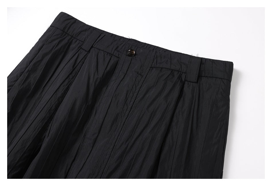 Close-up of the front waistband, button, belt loops, and pleats on black trousers.