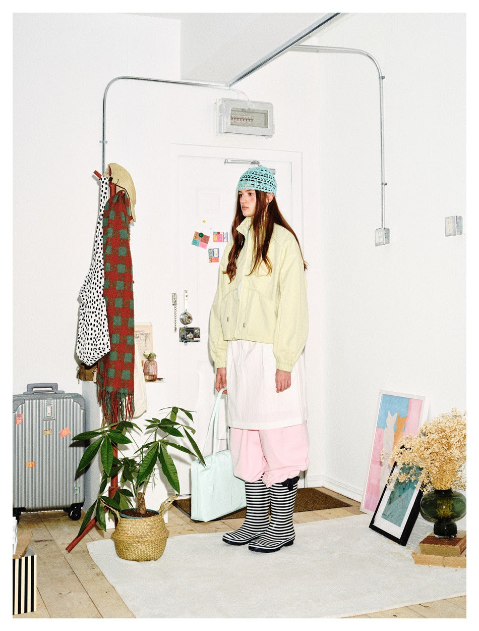 Model in profile wearing a pale yellow cropped jacket, white skirt, pink trousers and striped socks.