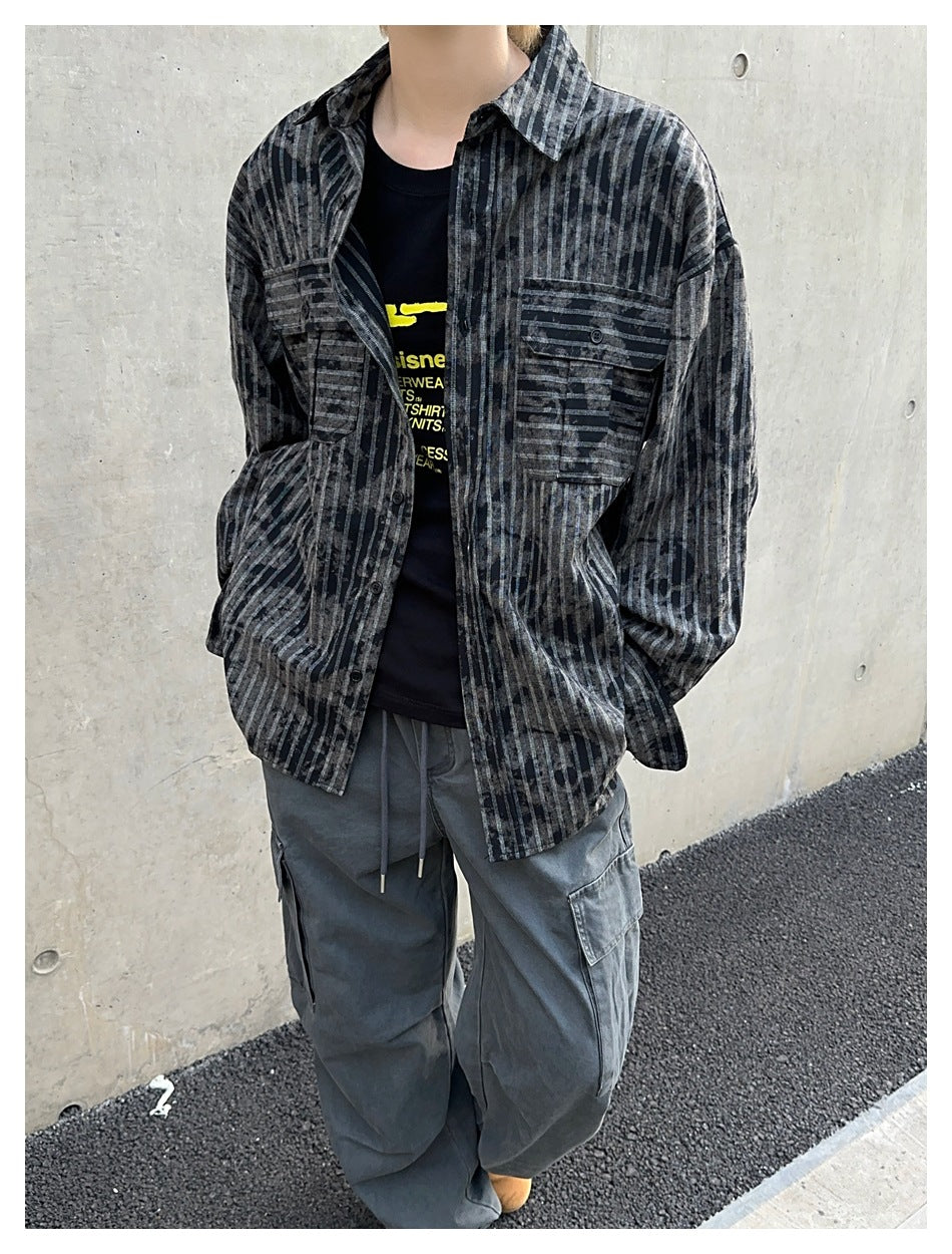 Close view of a person wearing an open charcoal striped button-up shirt with two flap chest pockets.