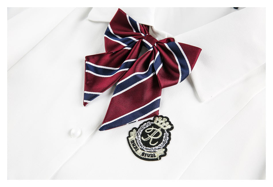 Close-up of the burgundy-and-navy striped bow and embroidered crest on a white shirt.