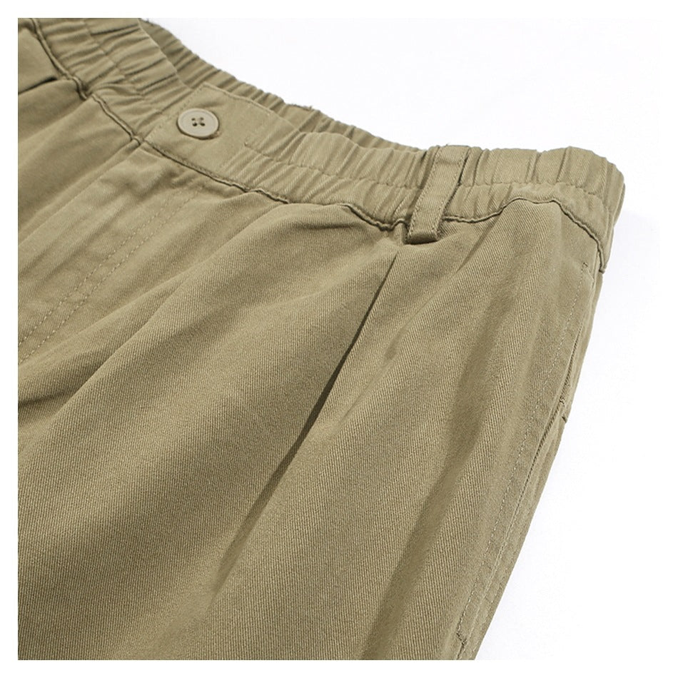 Angled close-up of khaki trousers showing the elastic waistband, button, belt loop and front pocket seam.
