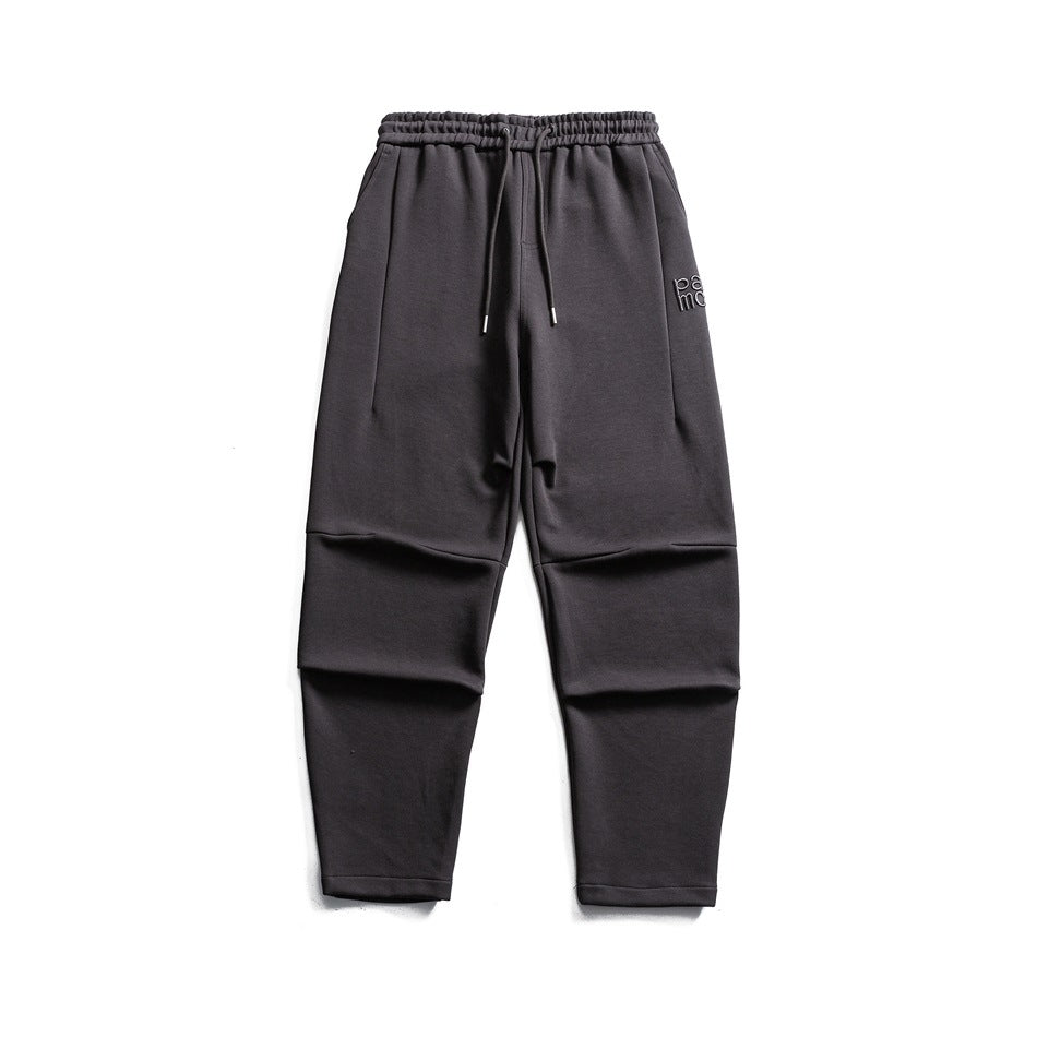 Charcoal gray knit drawstring sweatpants flat lay with knee pleats and a small logo on the thigh