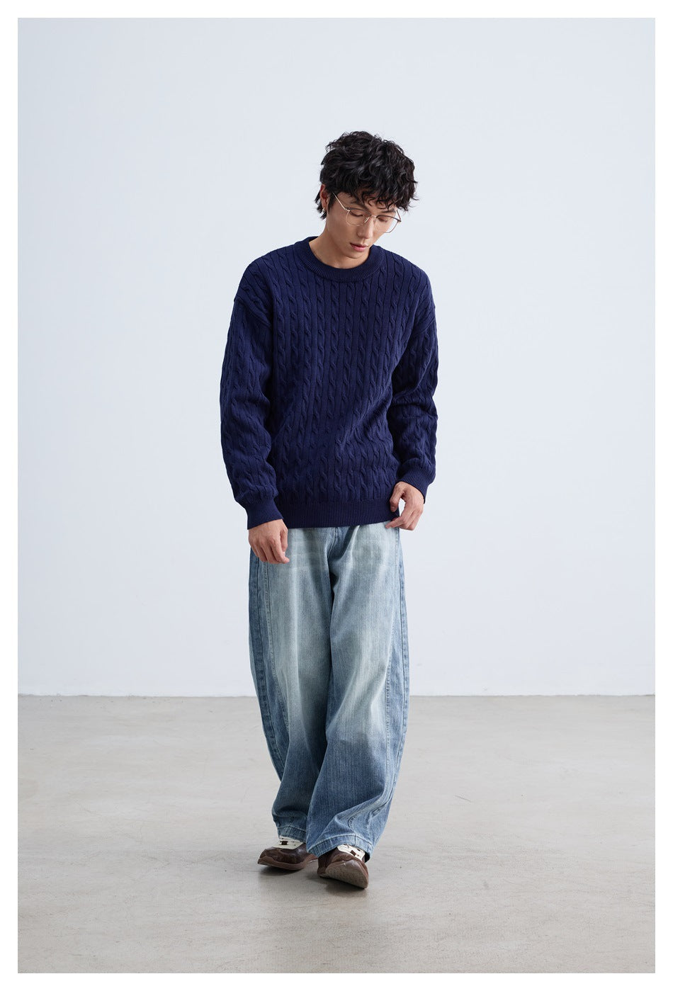 Full-length model wearing a navy cable-knit crewneck sweater and wide light-wash jeans.
