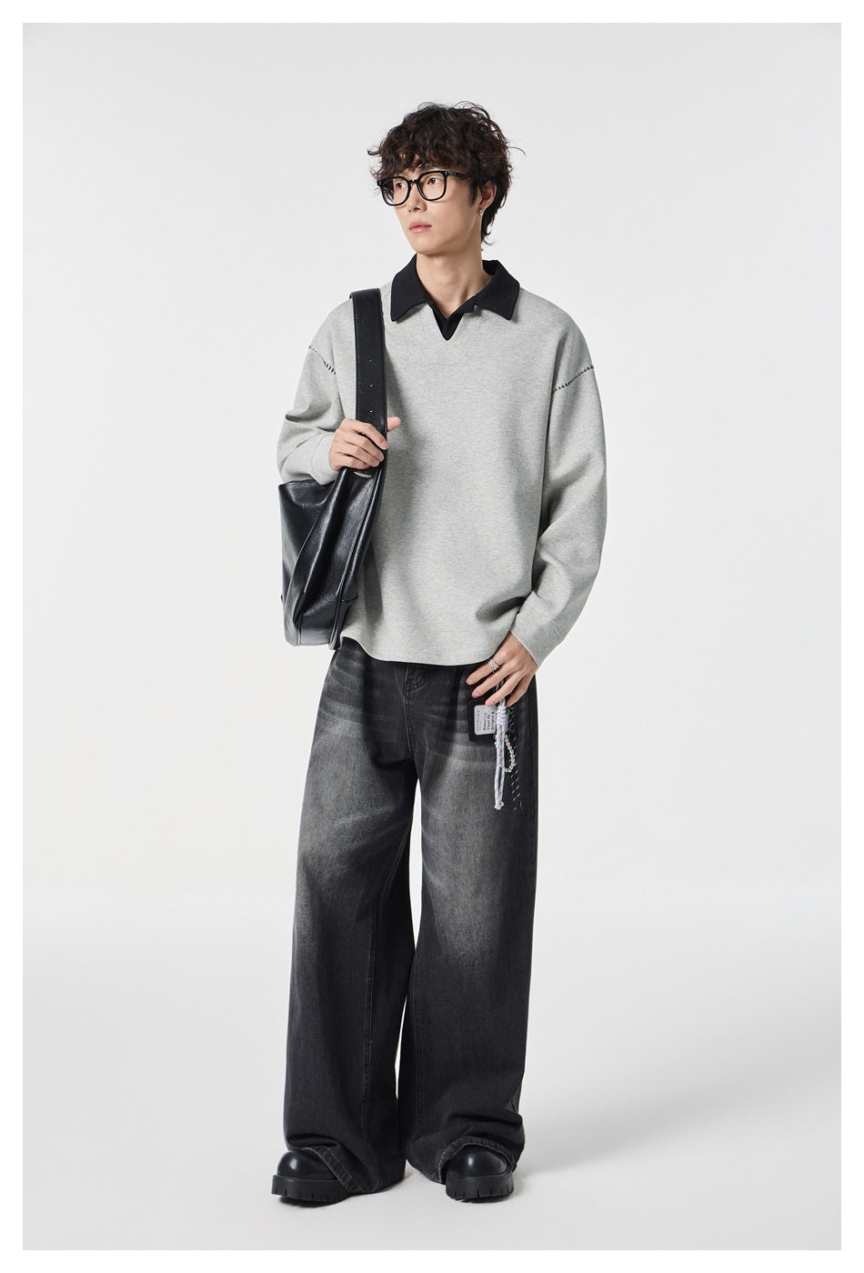 Model wearing a light gray pullover with black collar and shoulder stitching, carrying a black shoulder bag.