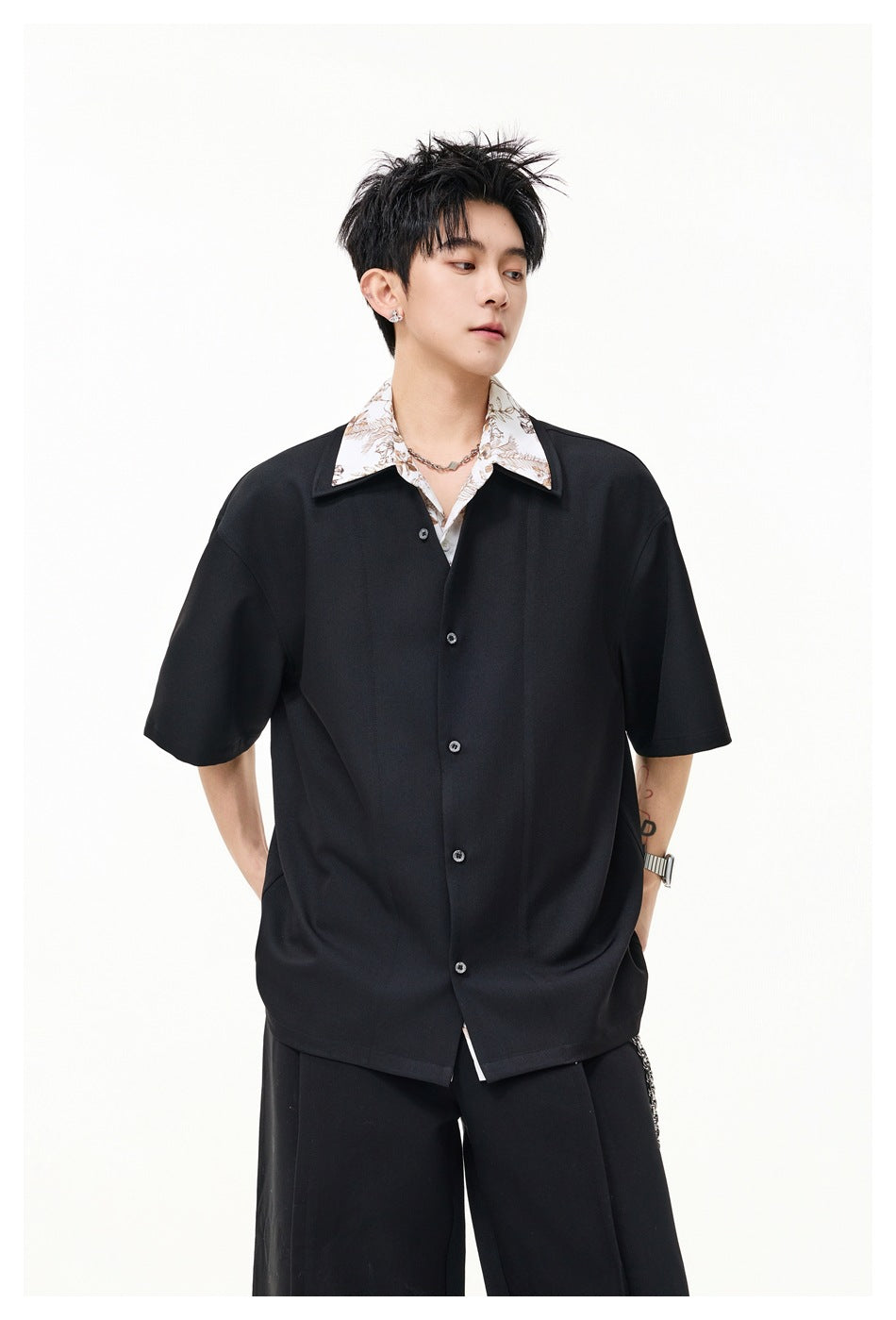 Model wearing a black short-sleeve button-front shirt with floral-print under-collar and black pleated trousers