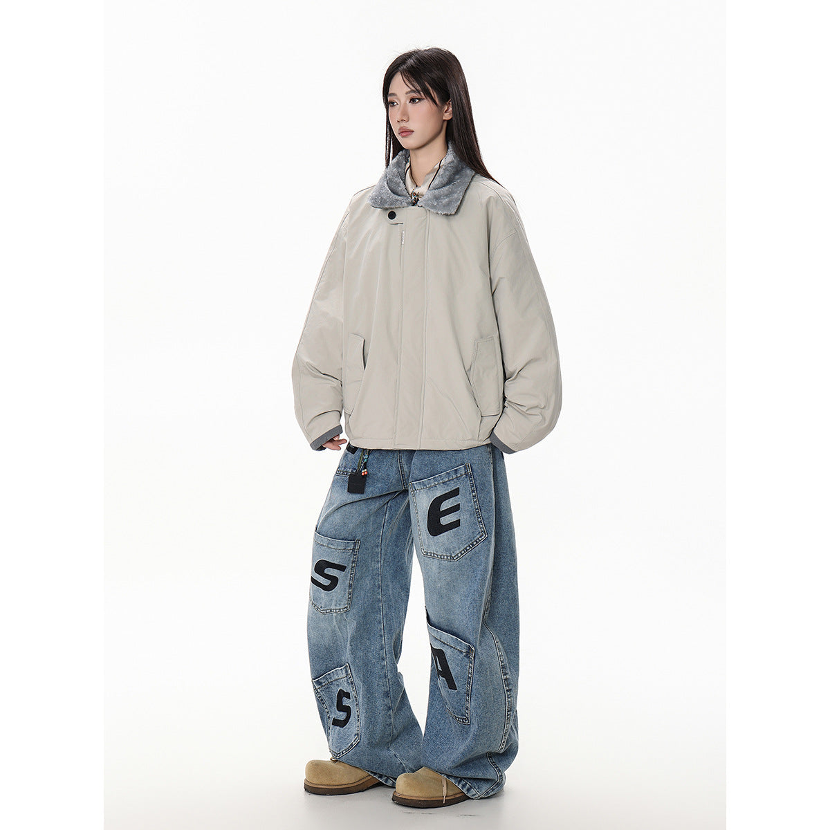 Model in a light gray oversized jacket with a gray plush collar and wide blue jeans with black letter patches.