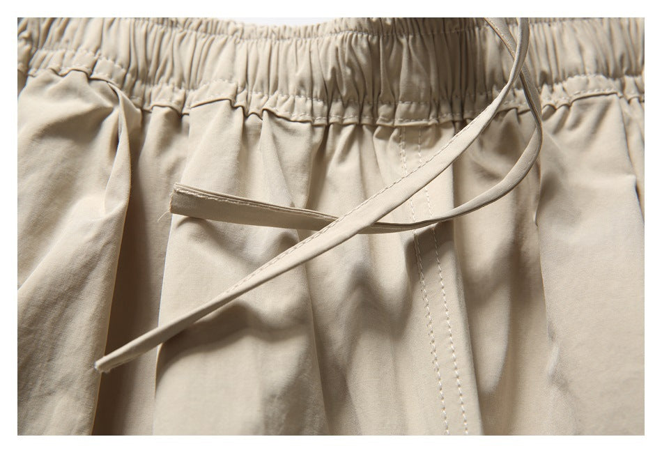 Close-up of beige trousers showing the gathered waistband, drawstring, and front stitching.
