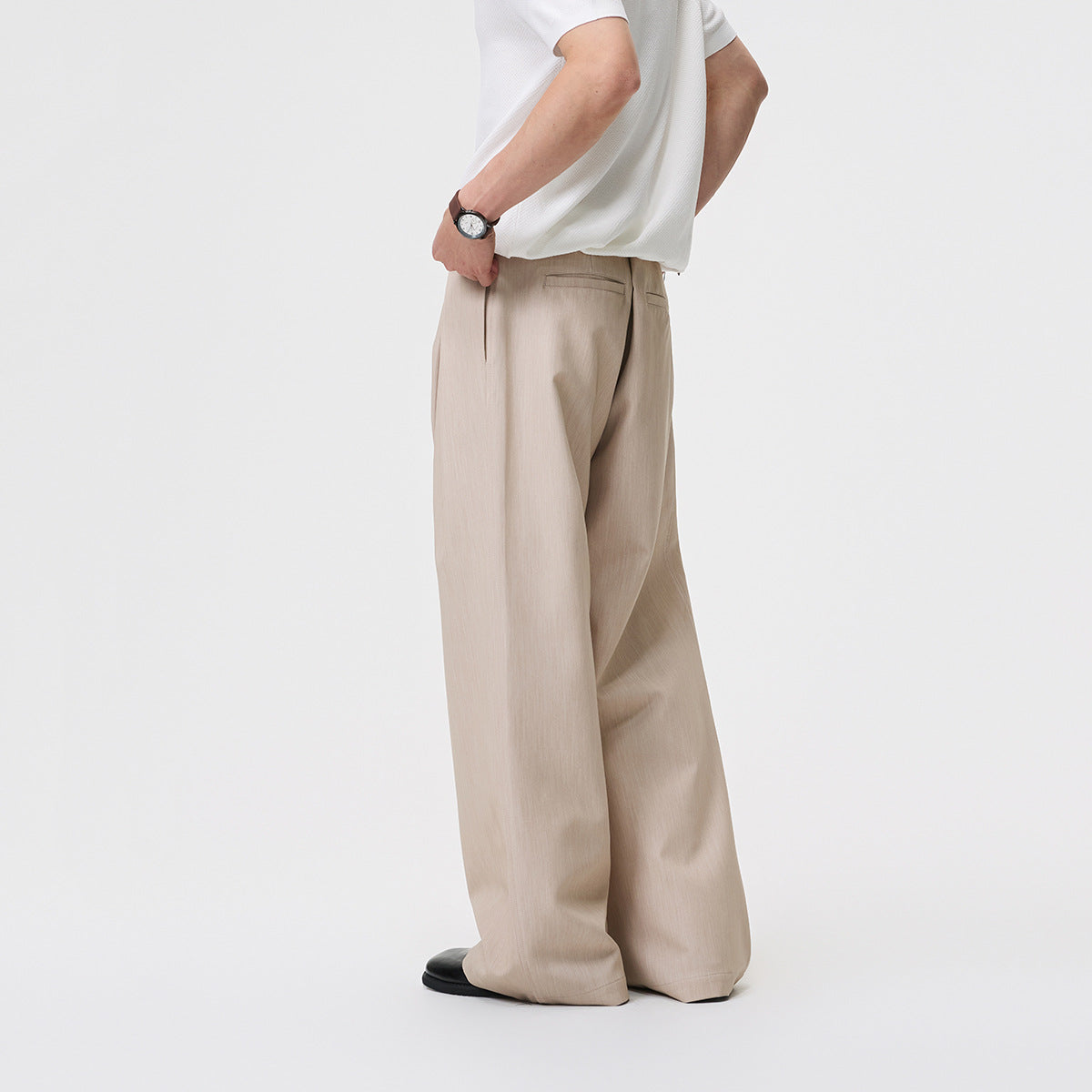 Model wearing beige wide-leg trousers, shown from the rear three-quarter angle with a back welt pocket.