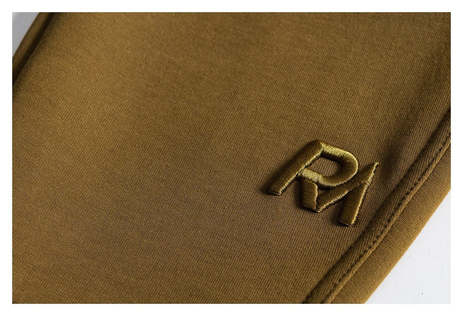 Close-up of olive-brown pants with a small raised tonal embroidered emblem.