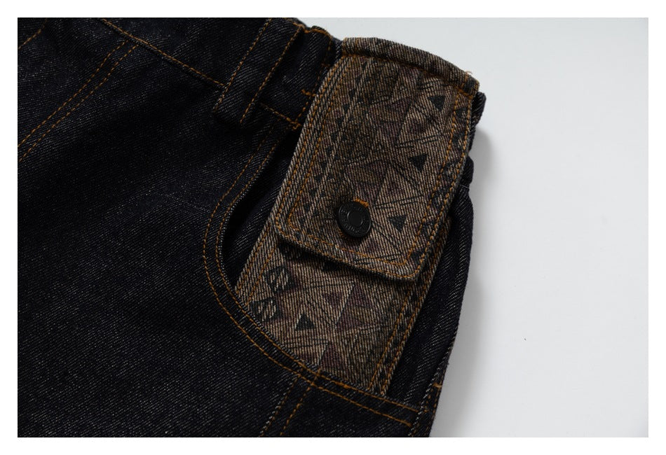 Close-up of black denim pants with a patterned fabric flap and dark button beside a curved pocket.