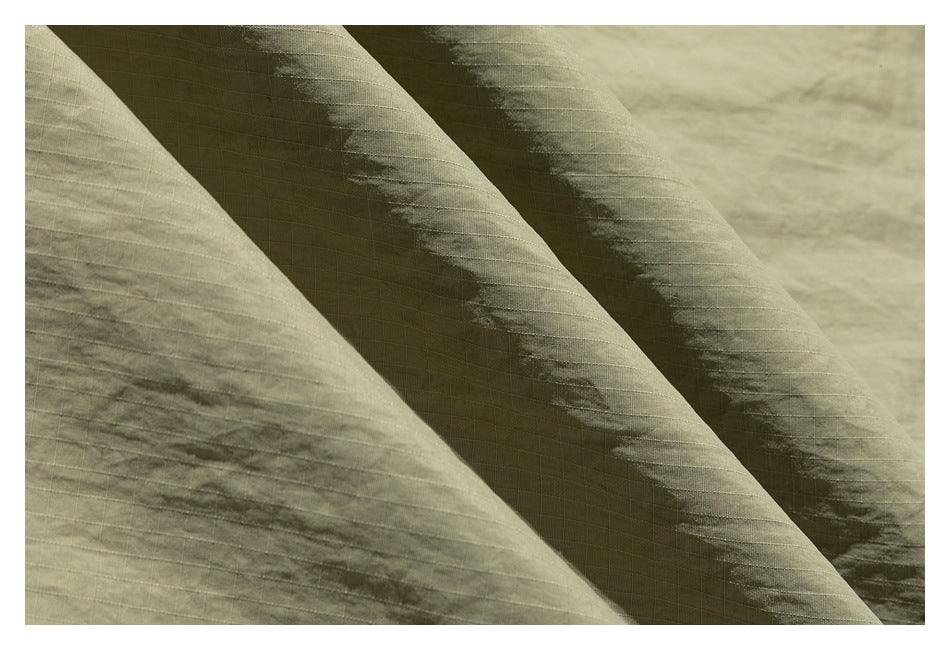 Close-up of olive-green garment fabric showing a subtle grid weave and creases.