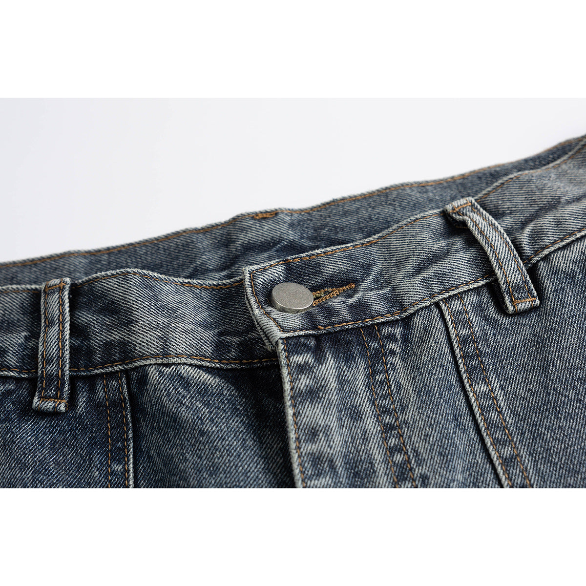Close-up of blue-gray washed jeans showing the waistband, belt loops, metal button, and fly stitching.
