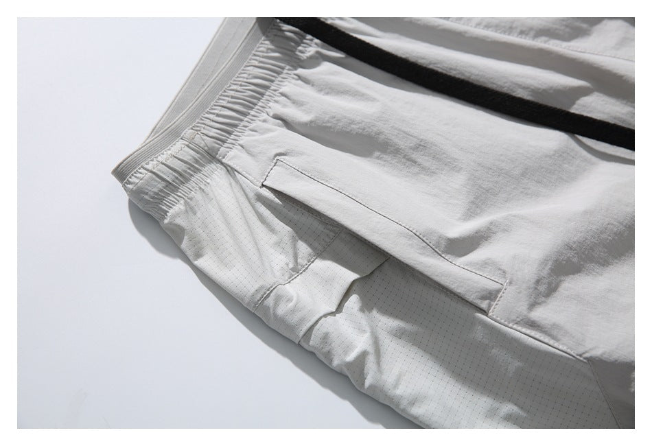 Close-up of light gray shorts with an elastic waistband, black drawcord, and angled side pocket.