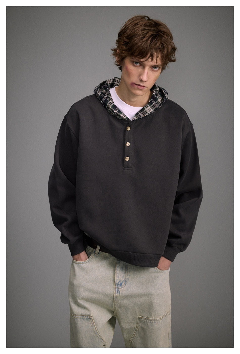 Man facing forward in a charcoal pullover with a plaid-lined hood and three-button placket.