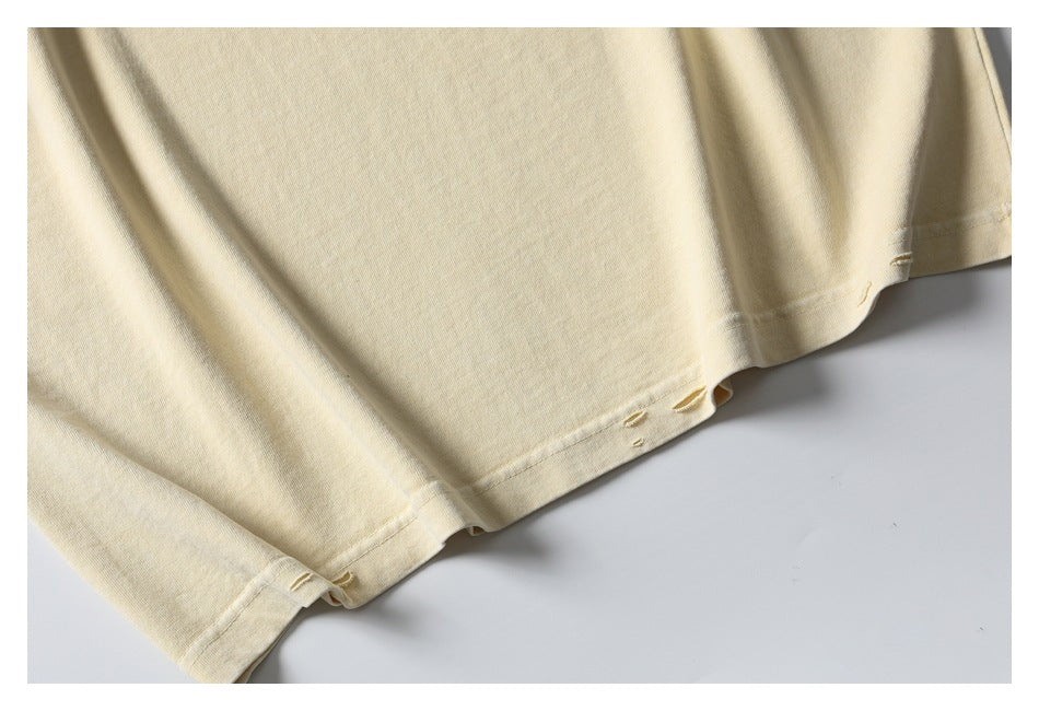 Close-up of the pale cream shirt's hem with small distressed slits and visible stitching.
