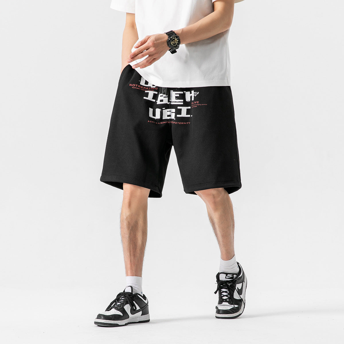 A model wears black knee-length shorts with a large white and red graphic across the front.