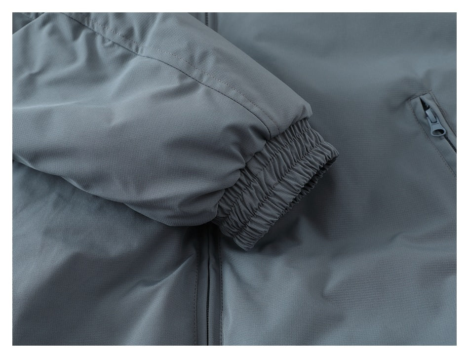 Close-up of a gathered elastic cuff beside a zip pocket on a gray jacket.
