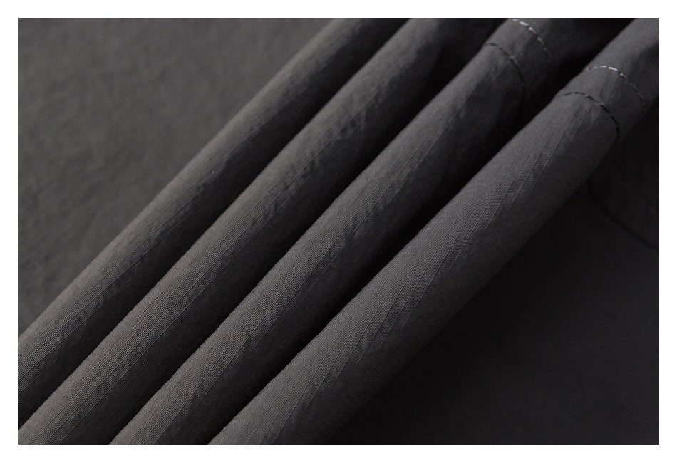 Close-up of charcoal gray fabric arranged in folds, showing its fine grid texture and stitching.