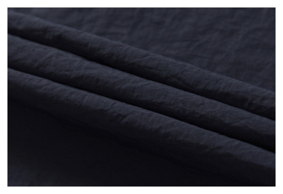 Macro view of dark navy garment fabric folded into soft ridges, showing its surface texture.