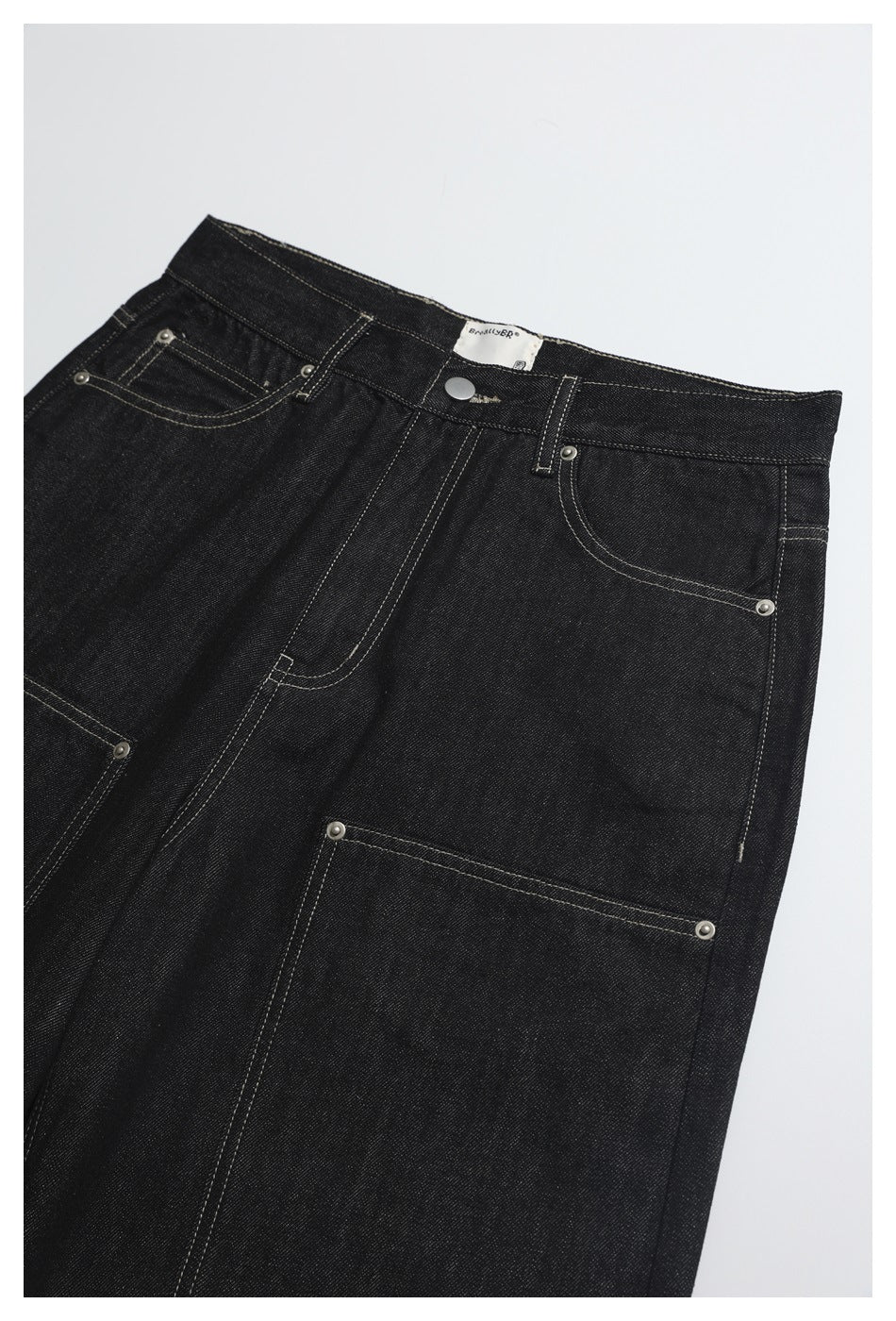 Close-up of black jeans showing the front waistband, pockets, metal rivets and large utility pocket.