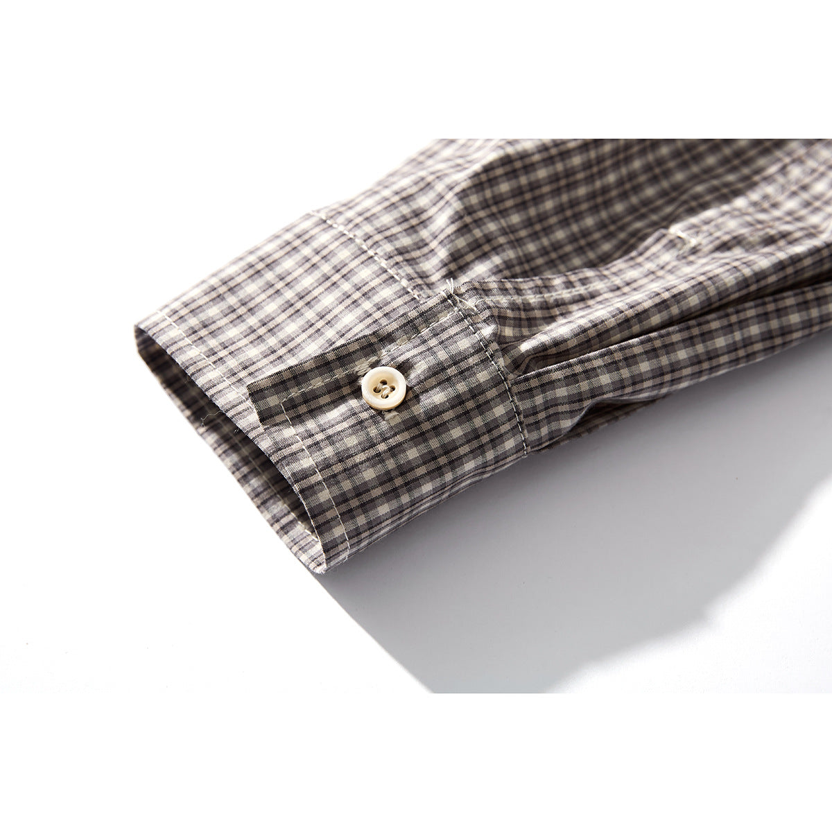 Close-up of a gray, black, and cream checked shirt cuff with a cream button.