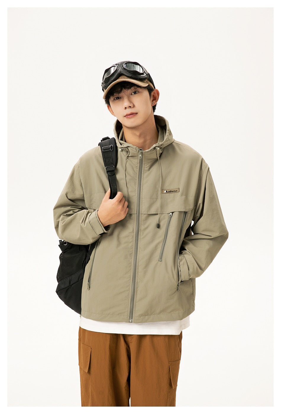 Model wearing a sage-gray hooded zip jacket with flap and zip pockets, shown with brown cargo pants.