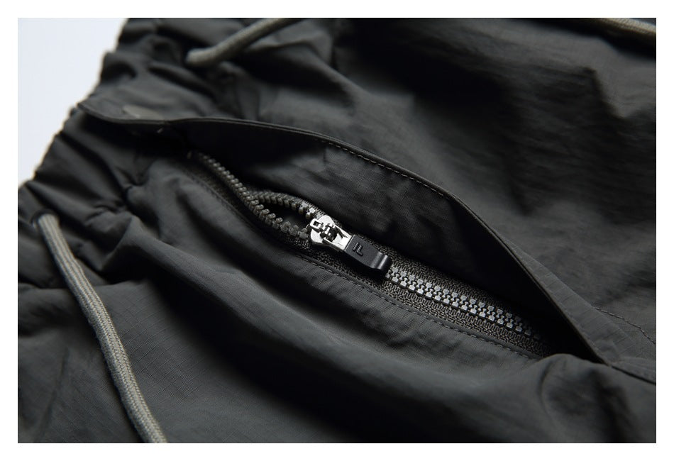 Close-up of charcoal shorts fabric with a black zipper beneath a flap.