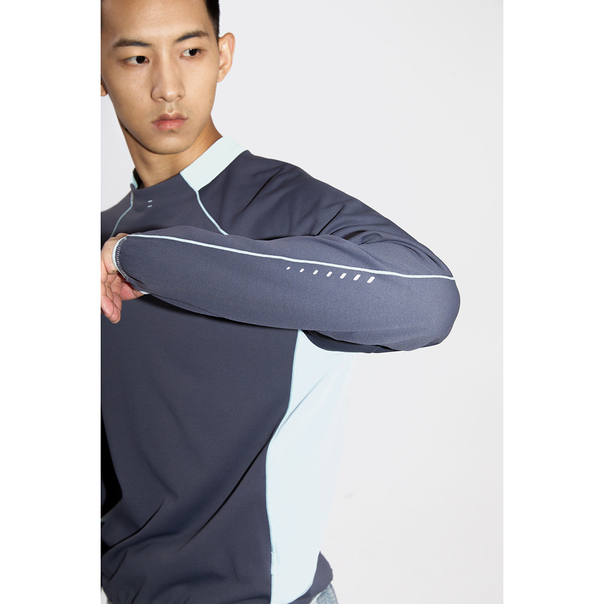 Close view of a man wearing a charcoal long-sleeve top with pale blue panels and piping.