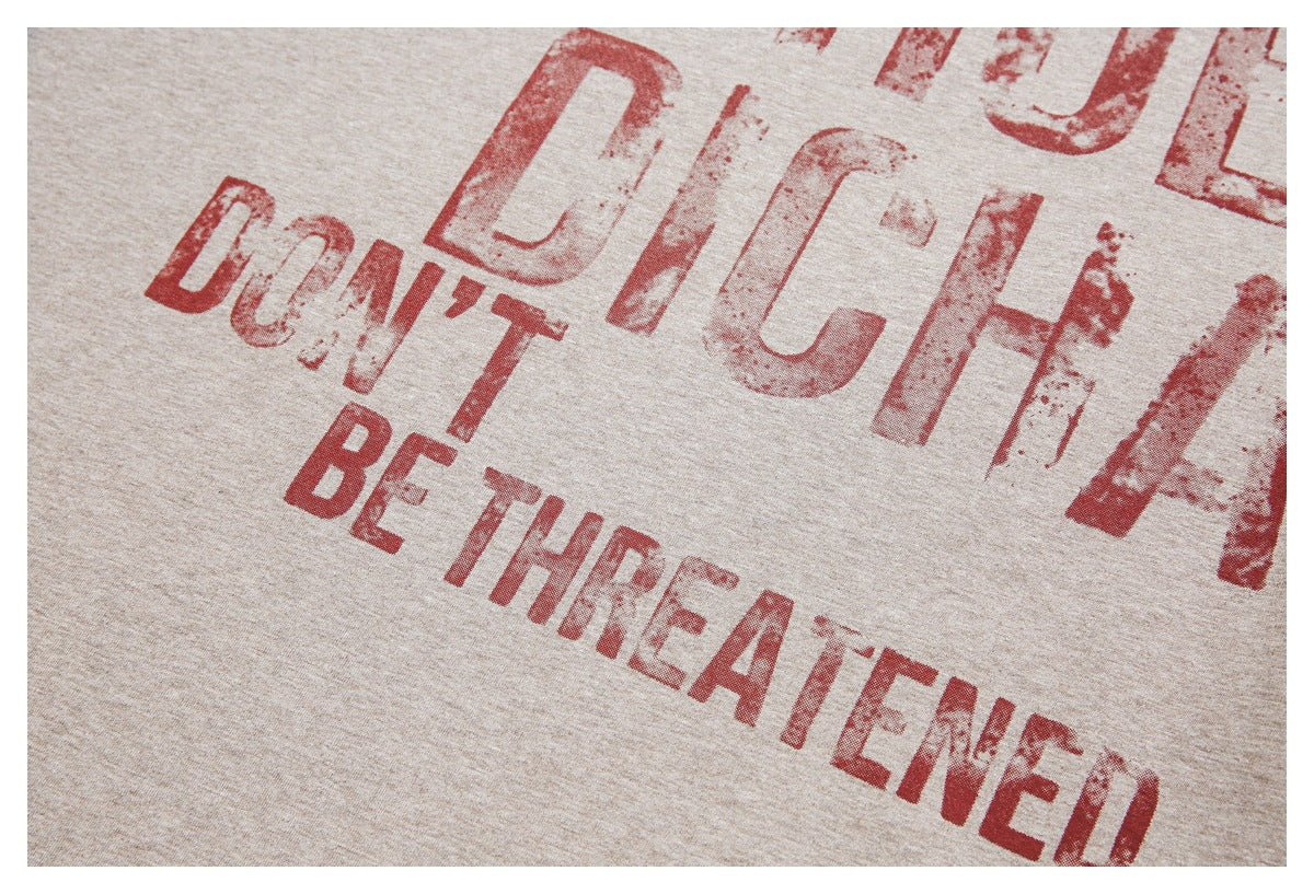 Close-up of distressed red English lettering printed across a beige heather T-shirt.