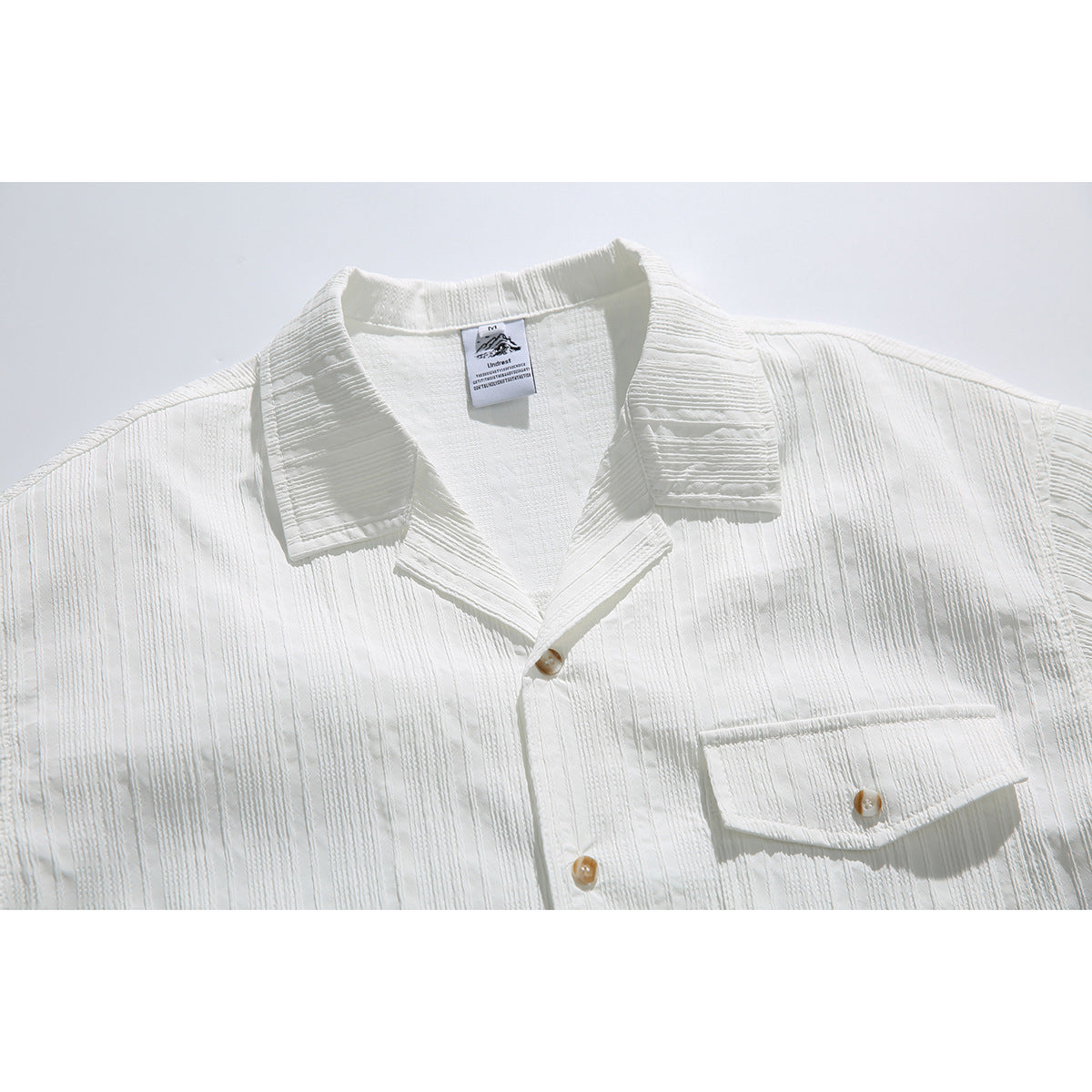 Close-up of a white short-sleeve shirt with a notched collar, tan buttons, a flap chest pocket, and raised vertical stripes.