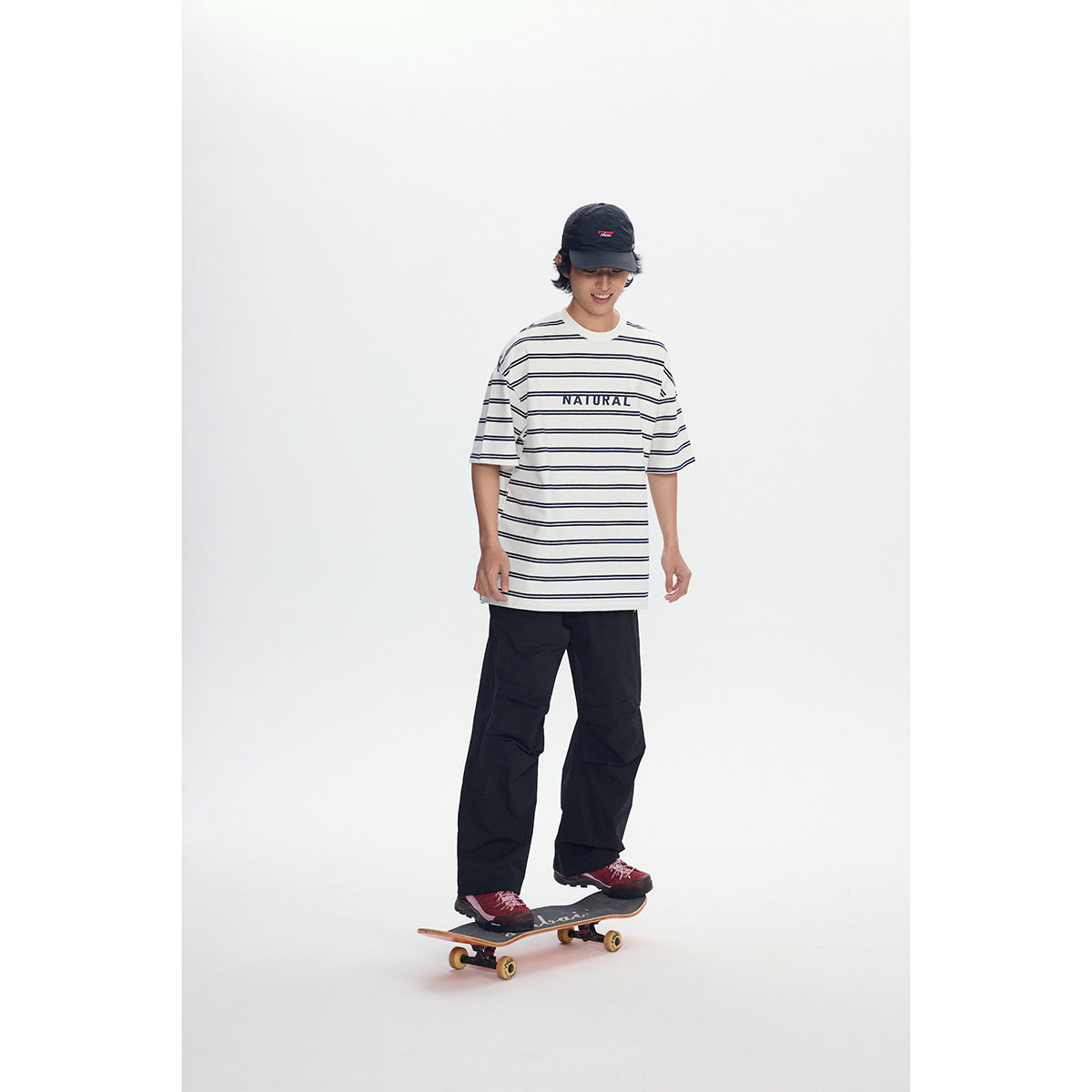 Full-length model wearing the striped ivory NATURAL T-shirt and black pants while balancing on a skateboard.